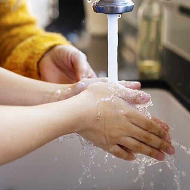 Un enfant se lave les mains sous un robinet et il est aidé par une autre personne.