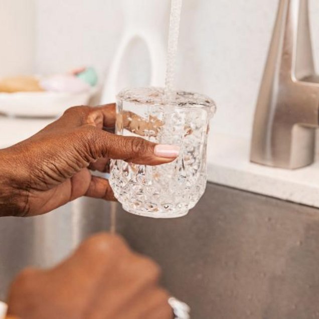 Une personne se serre un verre d'eau au robinet de sa cuisine.